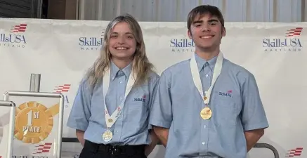 Christiansen and Often Take Gold - Carroll News | Carroll Publications | Carroll County, MD Two smiling SkillsUSA competitors wearing blue shirts with gold medals on stage beside a first-place sign.