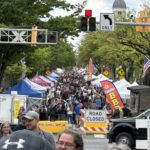 1778346497475-image-1 - Carroll News | Carroll Publications | Carroll County, MD Crowded street festival with vendor tents, American flags, and signs reading ROAD CLOSED along a tree-lined avenue.