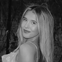 Black-and-white portrait of a smiling woman with shoulder-length hair outdoors, looking at the camera.