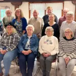 FarmMuseumVolunteers_featuredimage - Carroll News | Carroll Publications | Carroll County, MD Group of fourteen seniors posing for a photo in a bright community room, with seven seated in front and seven standing behind, casual attire.