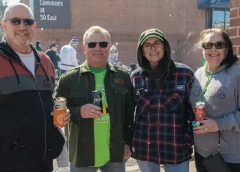 Four adults standing together outdoors at a community event, each holding a drink and smiling.