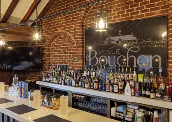 Brick-walled bar with wooden beams, a long white counter filled with assorted liquor bottles and a large Venue Bouchon sign on the brick wall behind.