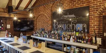 Brick-walled bar with wooden beams, a long white counter filled with assorted liquor bottles and a large Venue Bouchon sign on the brick wall behind.