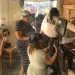 Group of people filming a video in a cafe, with a camera on a tripod and a monitor setup in the center of the scene.