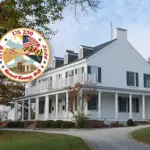 carroll-250-city-hall-featuredimagewebp - Carroll News | Carroll Publications | Carroll County, MD Large white historic house with a wraparound porch on a curved driveway, autumn trees, and an overlaid circular US 250 commemorative seal.