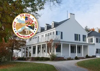 Large white historic house with a wraparound porch on a curved driveway, autumn trees, and an overlaid circular US 250 commemorative seal.