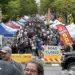 Crowded street festival with numerous vendor tents, American flags, and a road-closed barrier stretching along the avenue.