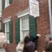 Crowd gathers outside a brick historic library building with green shutters and a hanging sign for Cockey's Helen B. Gorman Library of Carroll County History.