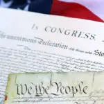 250th-westminster-reading-image - Carroll News | Carroll Publications | Carroll County, MD Close-up of the U.S. Declaration of Independence and a parchment reading 'We the People,' with an American flag in the background.