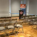 Auditorium-First-BLT-Set-up - Carroll News | Carroll Publications | Carroll County, MD Empty conference room with rows of brown folding chairs facing a podium and banner at the front of the room.