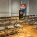 Auditorium-First-BLT-Set-up - Carroll News | Carroll Publications | Carroll County, MD Empty conference room with rows of brown folding chairs facing a podium and banner at the front of the room.