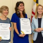 - Carroll News | Carroll Publications | Carroll County, MD Three women stand indoors, two in blue-toned dresses holding framed certificates and smiling as the third woman in a light blue blazer stands beside them.