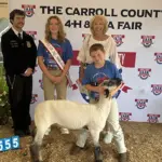corynne-FHfair - Carroll News | Carroll Publications | Carroll County, MD Group photo at a Carroll County 4-H Fair with a young girl wearing a sash, a boy with a sheep, a woman, and a uniformed official in front of a banner.