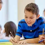 carroll-news-ccps-image - Carroll News | Carroll Publications | Carroll County, MD Group of four kids sit at a table, writing and drawing together in a bright classroom, smiling and helping each other on a project.